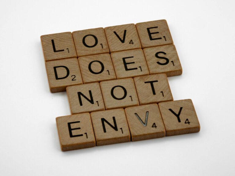 Inspirational quote 'Love does not envy' composed with Scrabble tiles on a white background.